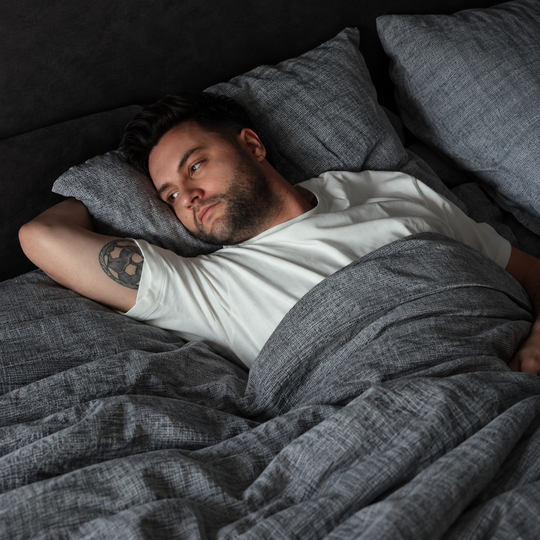 Man ligt wakker in bed onder een grijs dekbed