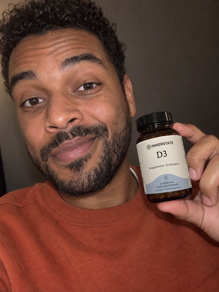 Man in een oranje shirt houdt een pot Innerstate vitamine D3 naast zijn gezicht