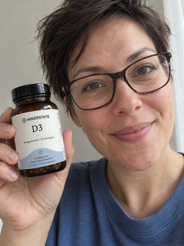 Vrouw met een bril houdt een pot Innerstate vitamine D3 naast haar gezicht