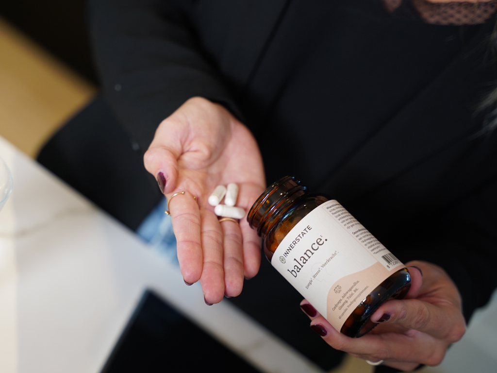 Hand met capsules en Innerstate Balance supplement in glazen pot